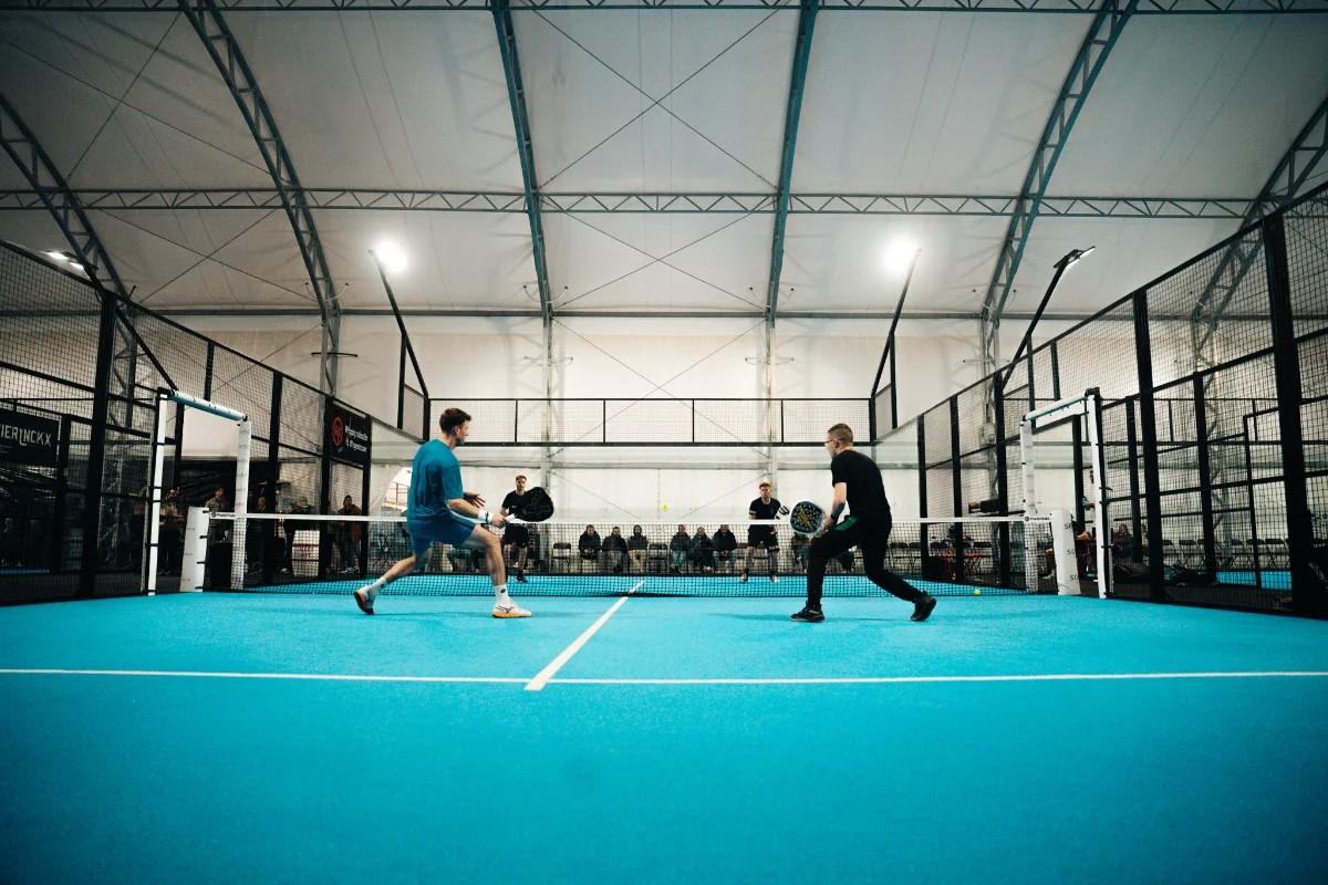 Dubbelmatch in een grote overdekte hal, spelers aan het net